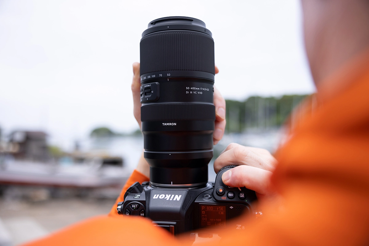 Photographe tenant un appareil Nikon Z avec l'objectif Tamron 50-400mm F/4.5-6.3 Di III VC VXD, capturant les détails et la polyvalence sur le terrain.