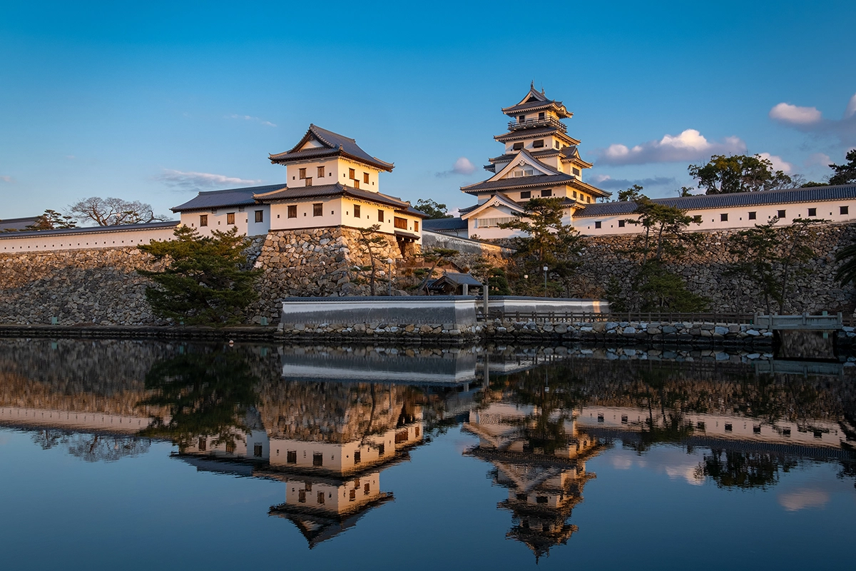Castelo japonês tradicional refletido em águas calmas na hora dourada, capturado com uma lente de viagem Tamron Fujifilm X-mount - mostrando detalhes arquitetônicos, precisão de cores e clareza na fotografia de viagem.