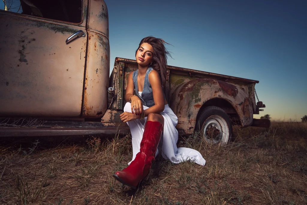 Una niña con botas rojas posaba delante de un camión viejo.