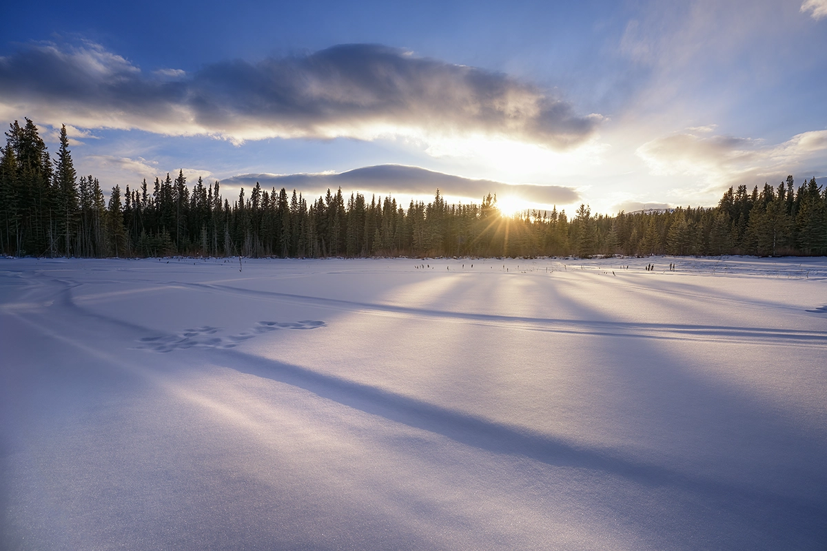O nascer do sol na hora dourada sobre a neve cheia de rastros de pneus e pegadas, capturado usando as melhores configurações para fotos do pôr e do nascer do sol.