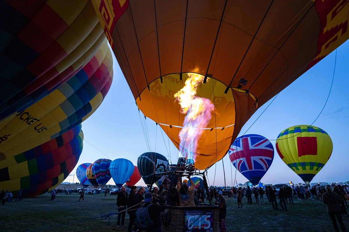 Balões de ar quente sendo inflados na hora azul, com chamas iluminando um balão.