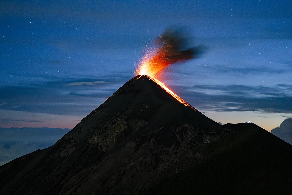 Vulcão em erupção com lava e fumaça durante a hora azul.