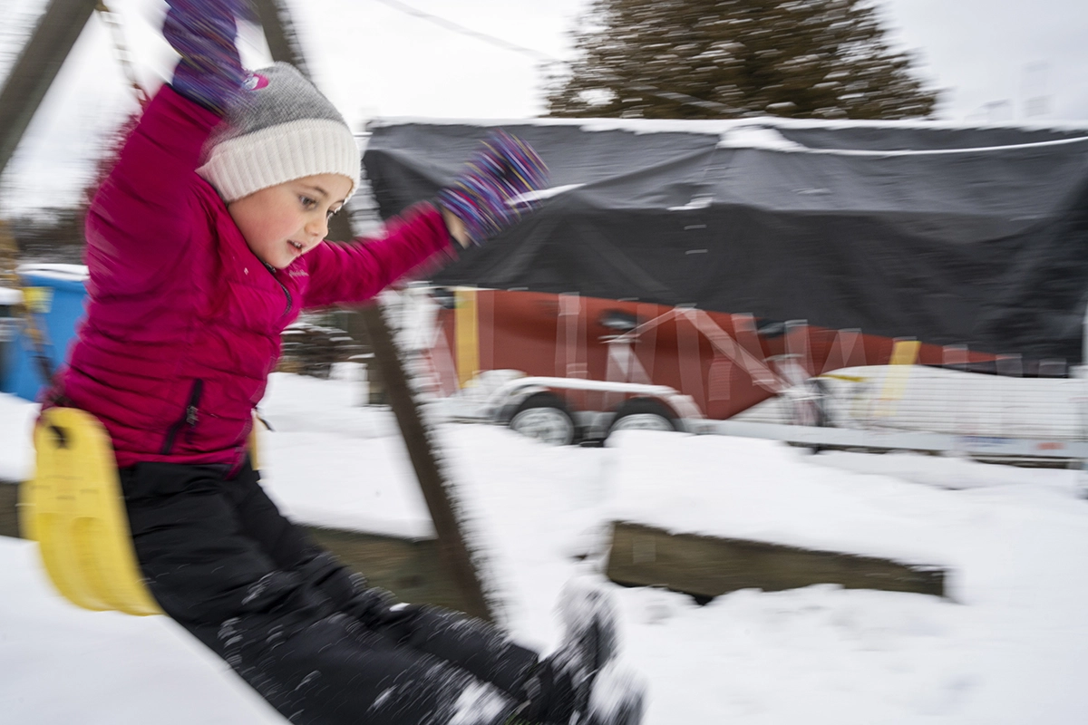 Panning photography of a child on a swing in winter, showing motion blur background and sharp subject to demonstrate the panning technique.