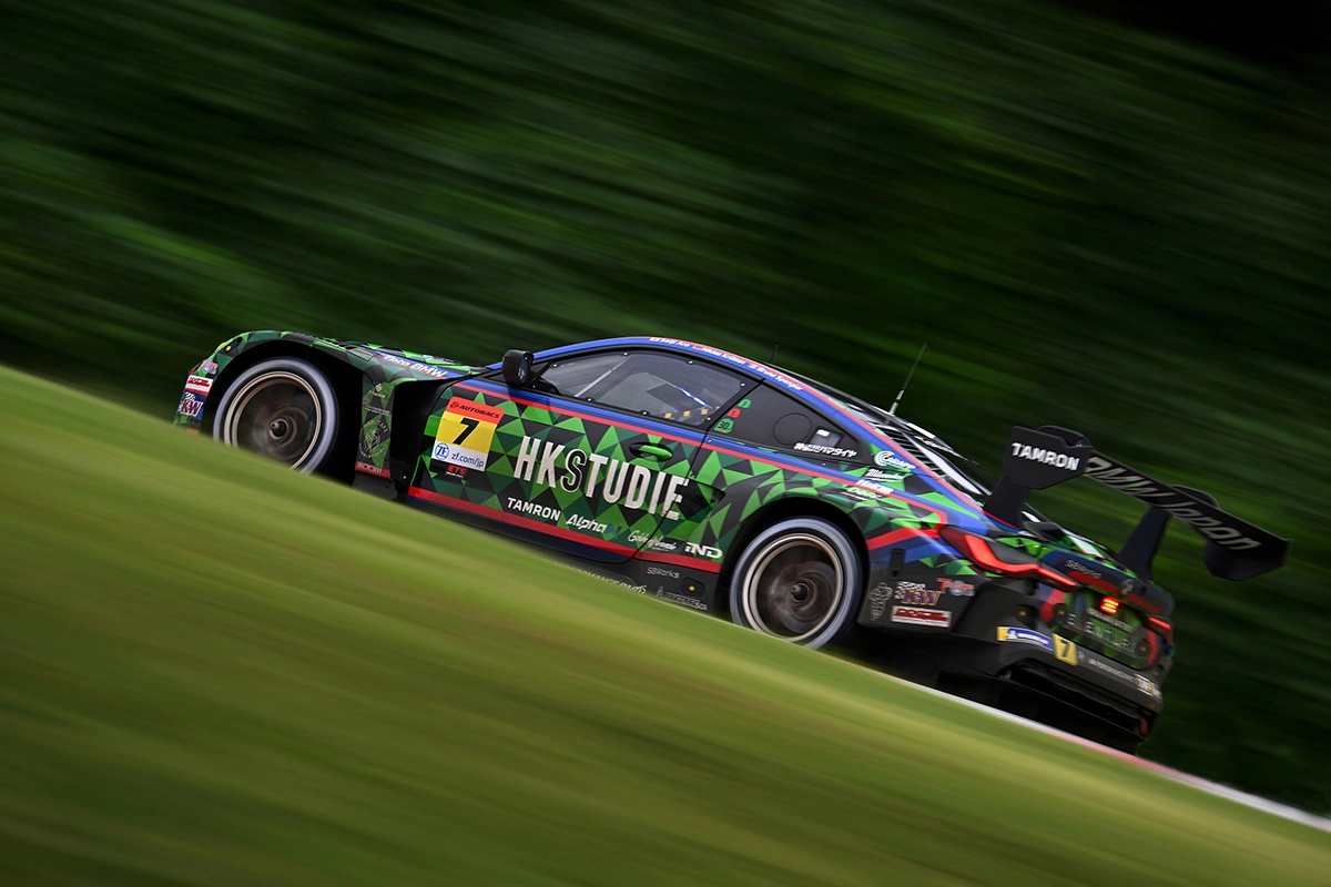 Carro de corrida colorido acelerando em uma pista, capturado com uma técnica de panorâmica, mostrando detalhes nítidos do veículo contra um fundo verde desfocado por movimento.