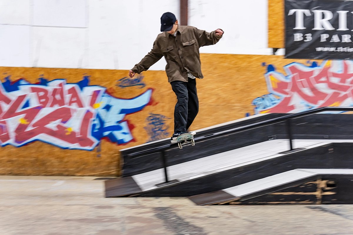 Panning photography of a skateboarder grinding a rail in an indoor skate park, with motion blur background emphasizing speed and balance.