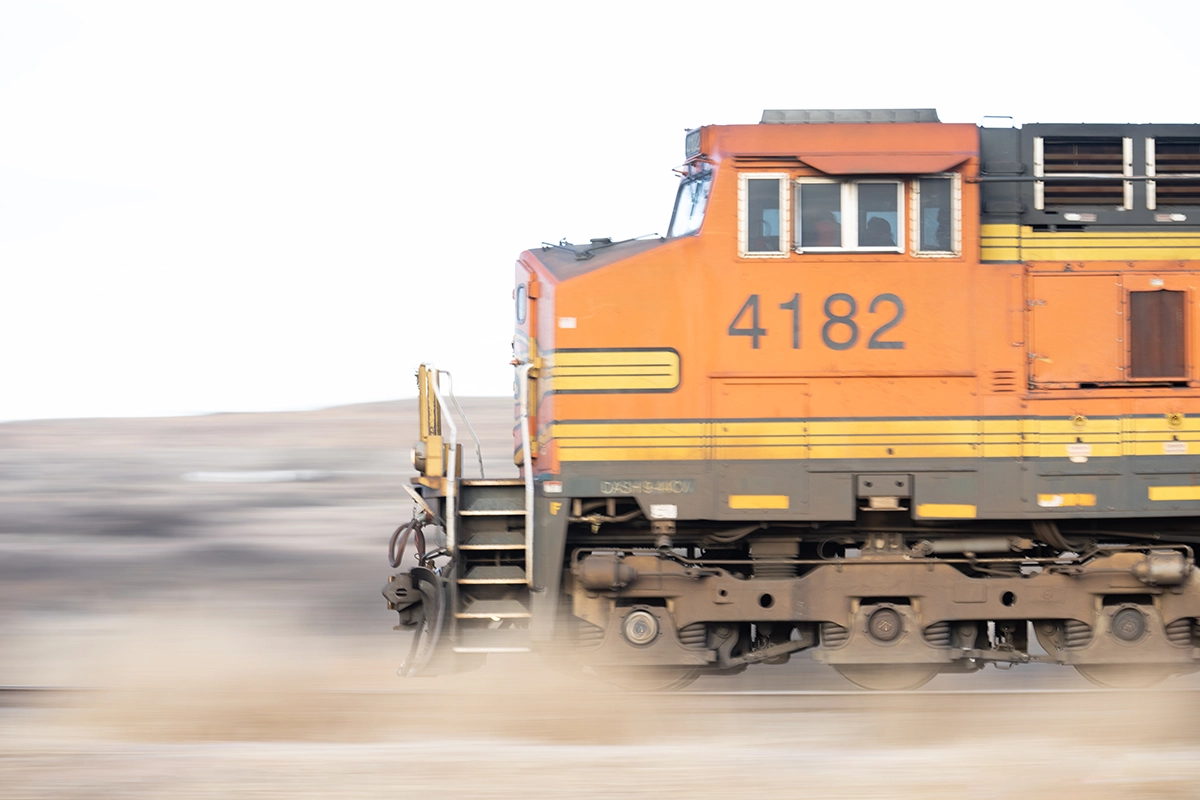 Orange freight train in motion captured with a panning technique, showing a sharp train against a blurred background to convey speed.