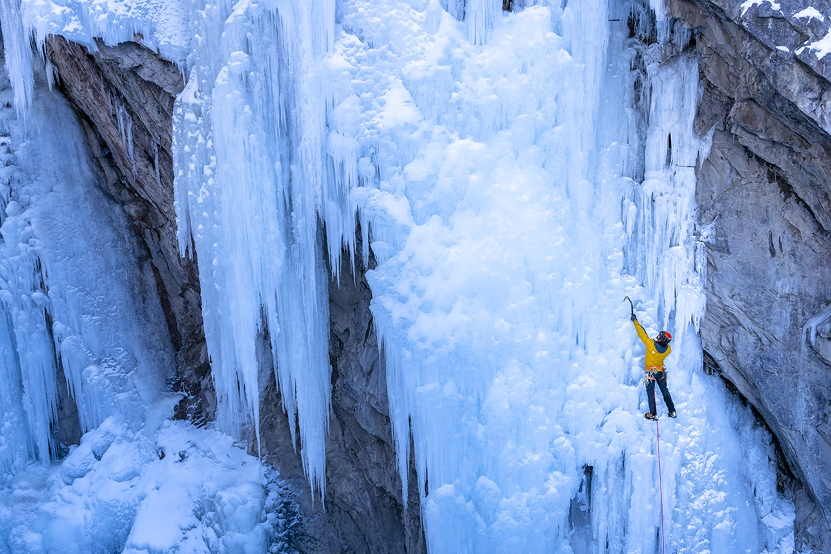 A yellow-clad ice climber scaling a wall of shimmering blue ice in Ouray’s famous Ice Park.