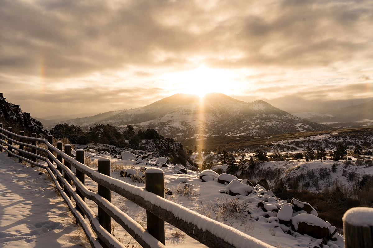 A serene sunrise image of a fence leading toward snow-dusted peaks near Ridgway.