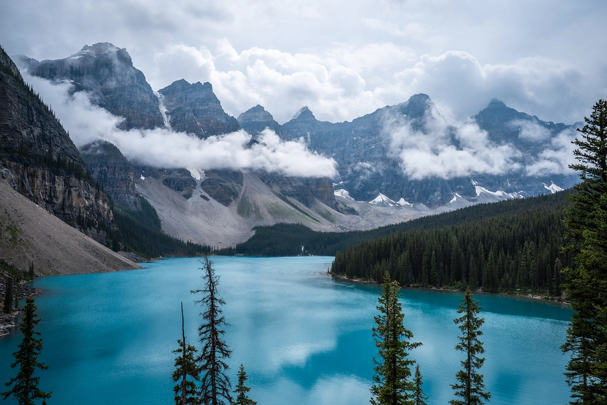 Vivid turquoise lake surrounded by evergreen forests and snow-capped peaks under a cloudy sky, captured with the Tamron 28-75mm F2.8 G2 lens highlighting crisp detail and natural color rendering.
