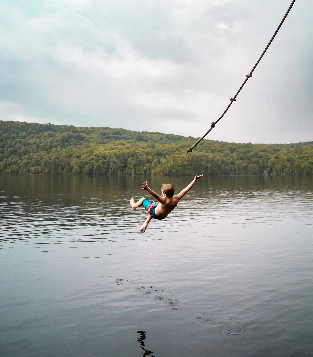 Boy mid-air after jumping from a rope swing over a calm lake, captured with the Tamron 28-75 G2 showcasing the precise autofocus motor.