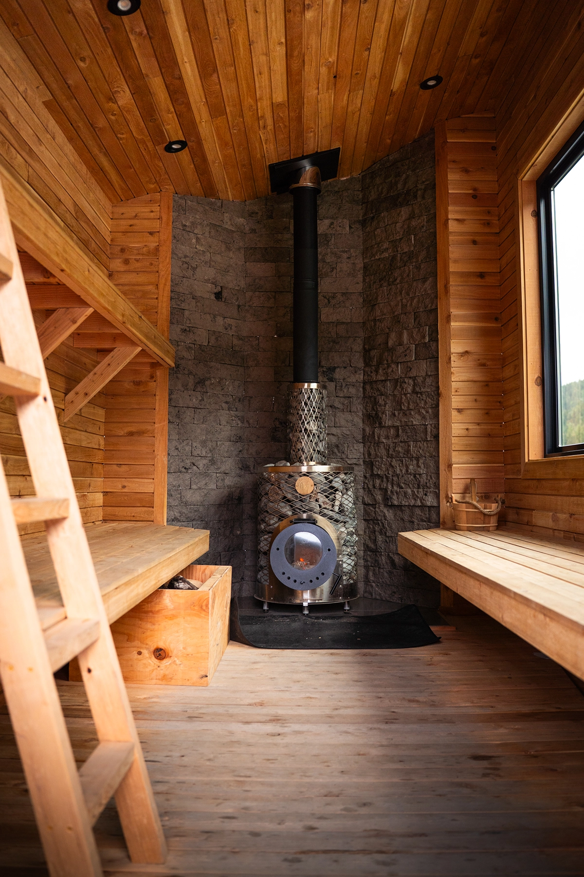 Warm wooden sauna interior with a metal wood-burning stove against a stone wall, photographed with the Tamron 28-75mm F2.8 G2 lens to capture images in extreme conditions.