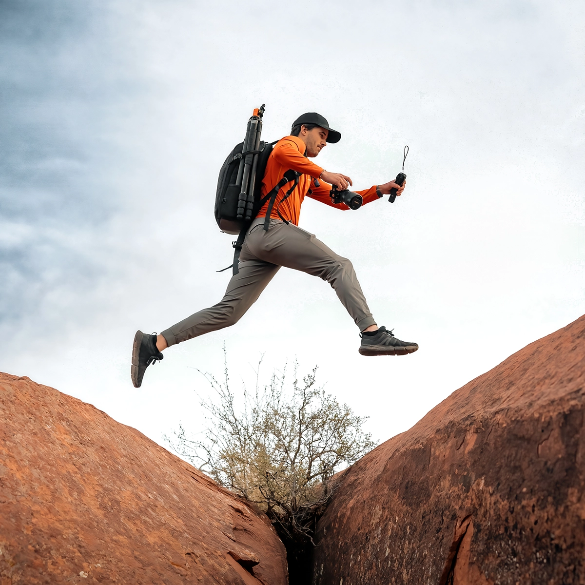 Photo from a low angle of Seth Macey jumping over rocks with a backpack of gear and his camera and Tamron lens in hand.