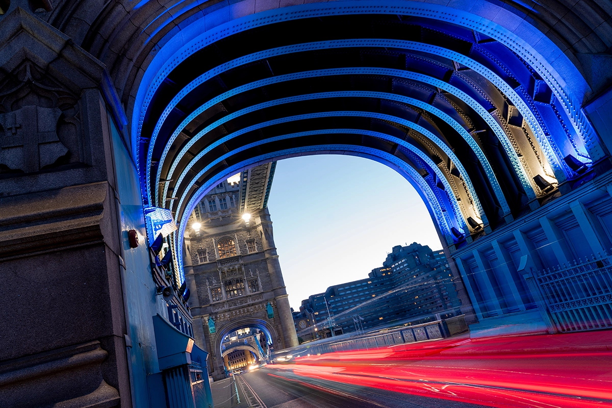 Pont urbain au crépuscule photographié avec un temps d'exposition long, montrant les traînées lumineuses rouges des voitures et l'architecture illuminée de bleu.