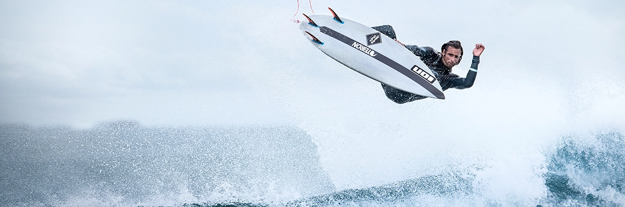 Surfista realizando una maniobra aérea capturada con una velocidad de obturación rápida, mostrando la técnica fotográfica de congelación del movimiento y acción.