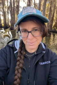 Portrait de la photographe naturaliste Alyce Bender dans un marais du sud, vêtue d'une veste Tamron alors qu'elle photographie les zones humides.