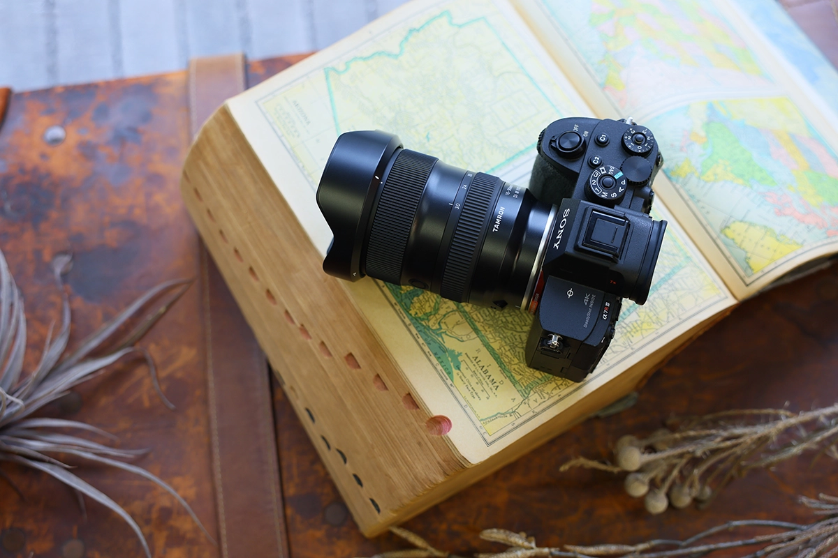 Tamron 16-30 mm F2.8 Di III VXD G2 monté sur un appareil photo sans miroir Sony, présenté sur un atlas ouvert pour une configuration de photographie de voyage.