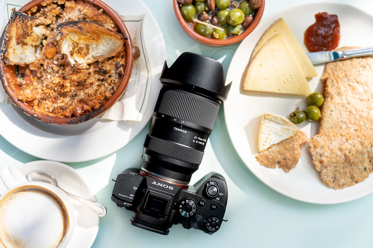 Lente Tamron 28-75 mm F2.8 G2 em uma câmera sem espelho da Sony fotografada em uma mesa de café com comida, mostrando o uso no estilo de vida real.