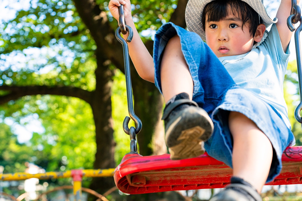 Criança balançando para a frente em um balanço vermelho de playground, fotografada com a Tamron 28-75 mm F2.8 G2 durante o recreio da família ao ar livre.