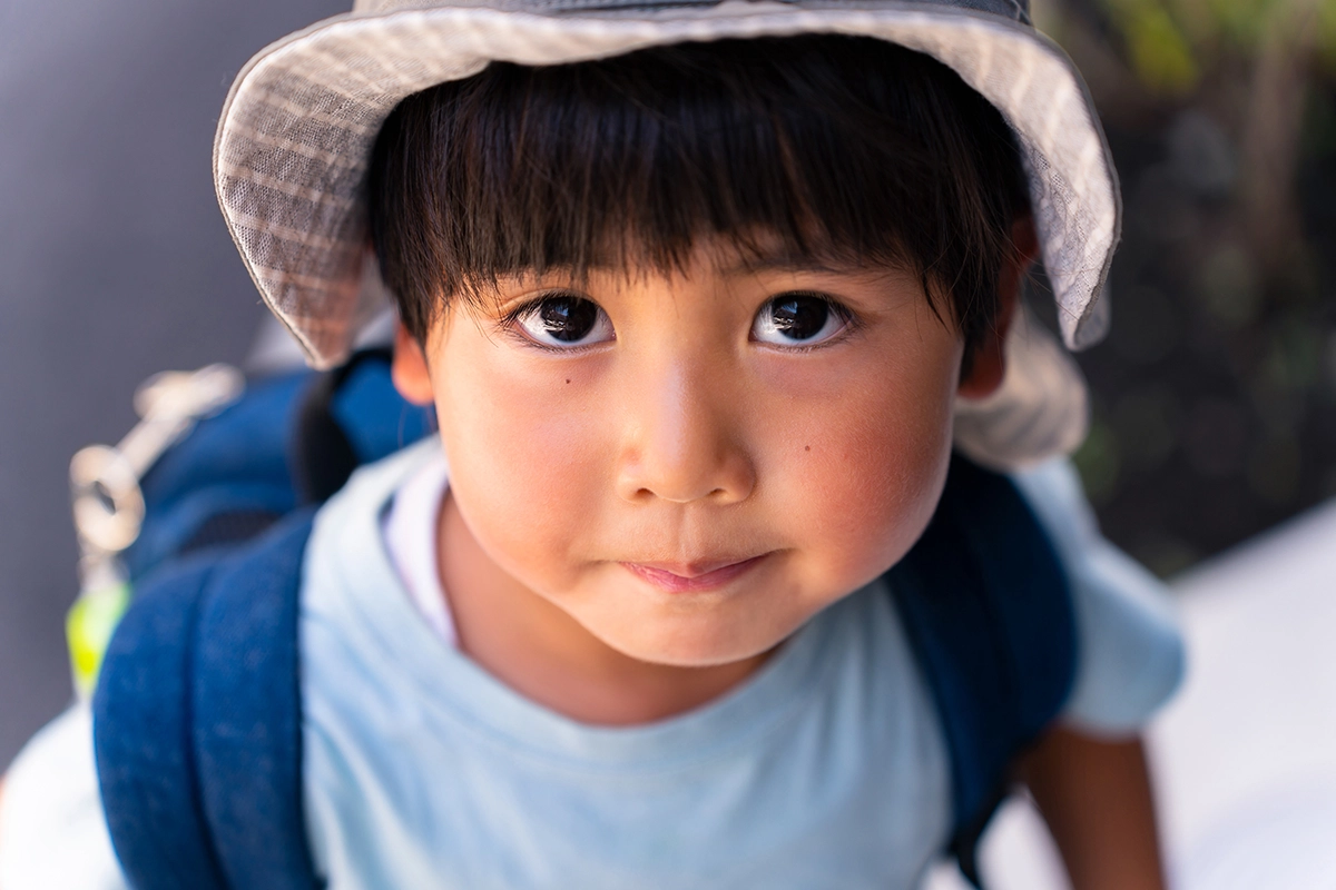 Retrato externo em close-up de um garoto usando chapéu e mochila, fotografado com a Tamron 28-75 mm F2.8 G2 para fotografia de retrato de família.