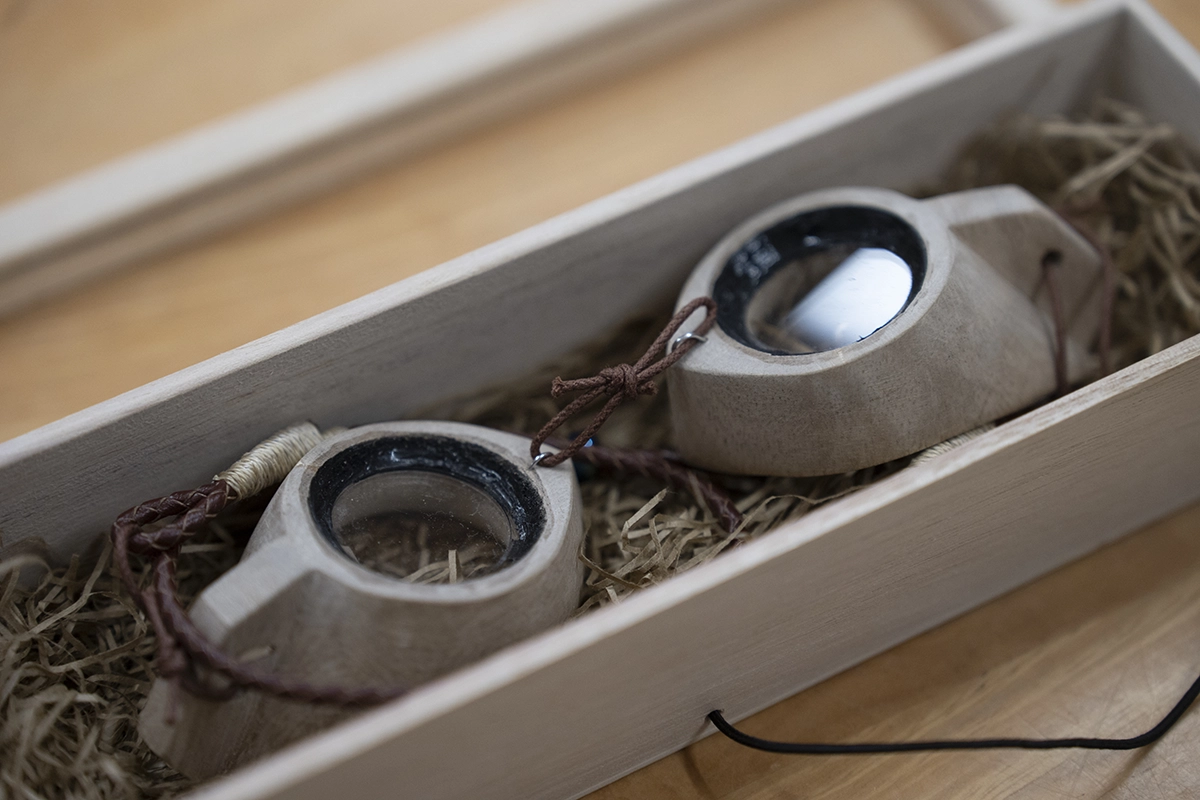 Close-up de óculos MIIKAGAN feitos à mão em Okinawa em uma caixa de madeira, fotografados com a Tamron 28-75mm F2.8 G2 para destacar o artesanato cultural em um documentário de narrativa visual.