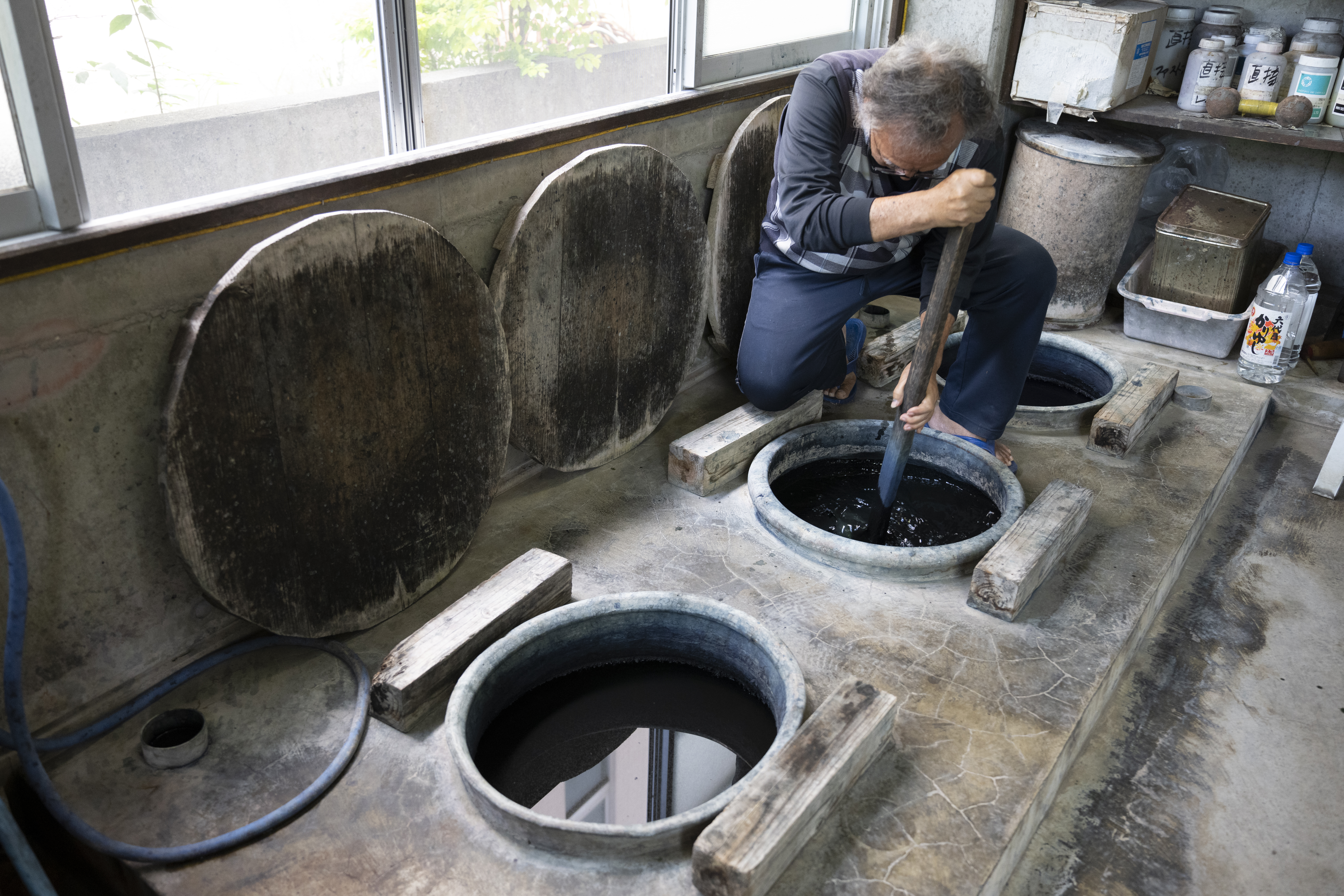 Artesão de Ryukyu Kasuri mexendo em tanques de tingimento em uma oficina tradicional de Okinawa, fotografado com a Tamron 28-75mm F2.8 G2 para um projeto de documentário de narrativa visual.