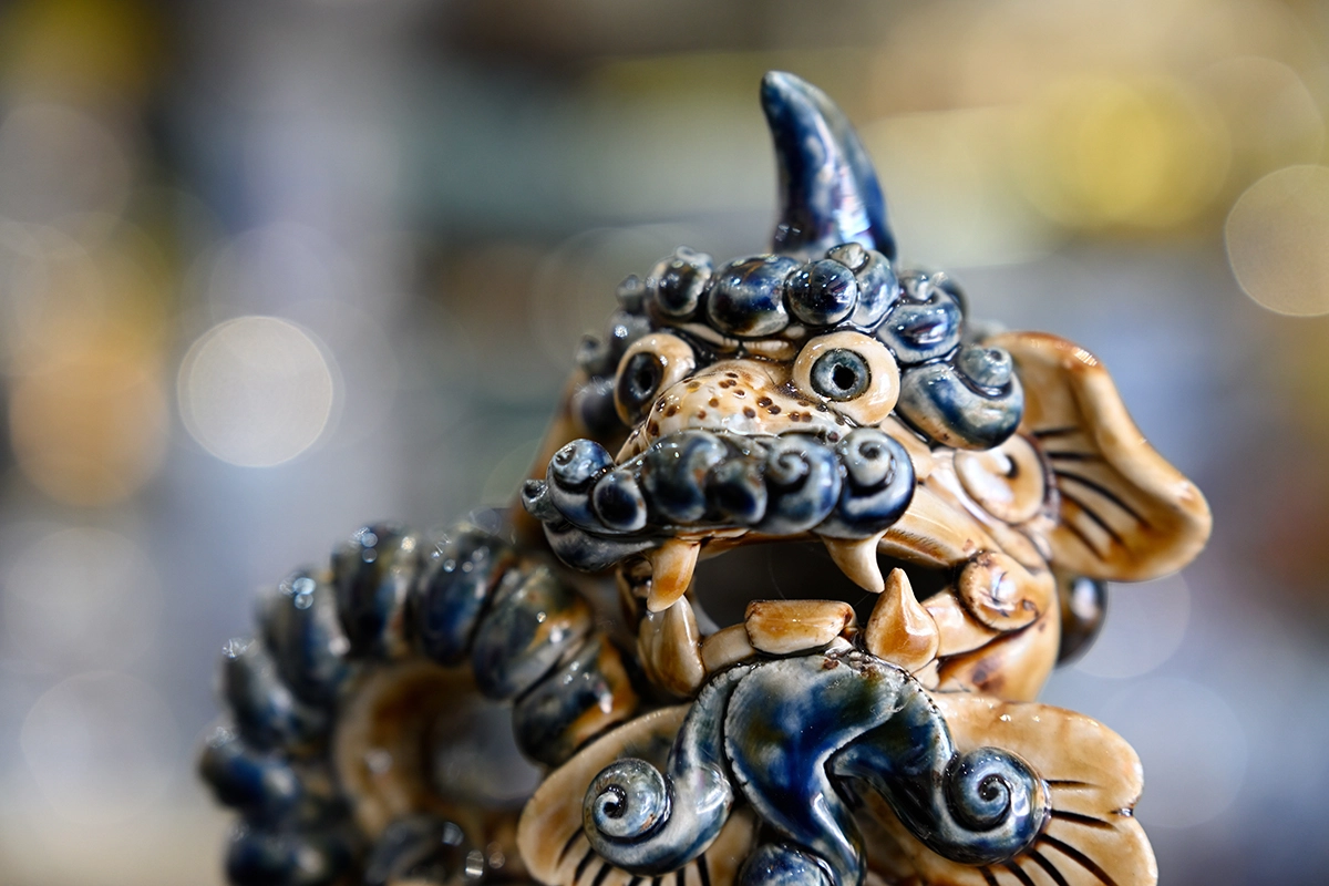 Close-up de uma estatueta artesanal de leão em cerâmica da vila de cerâmica de Bát Tràng, com bokeh circular suave atrás dela, fotografada com a Tamron 28-75 mm F2.8 G2.