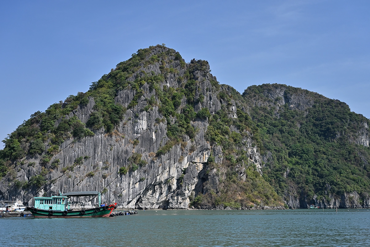 Penhascos íngremes de calcário erguendo-se acima da água calma em Hạ Long Bay com um barco tradicional vietnamita, fotografado com a Tamron 28-75 mm F2.8 G2.