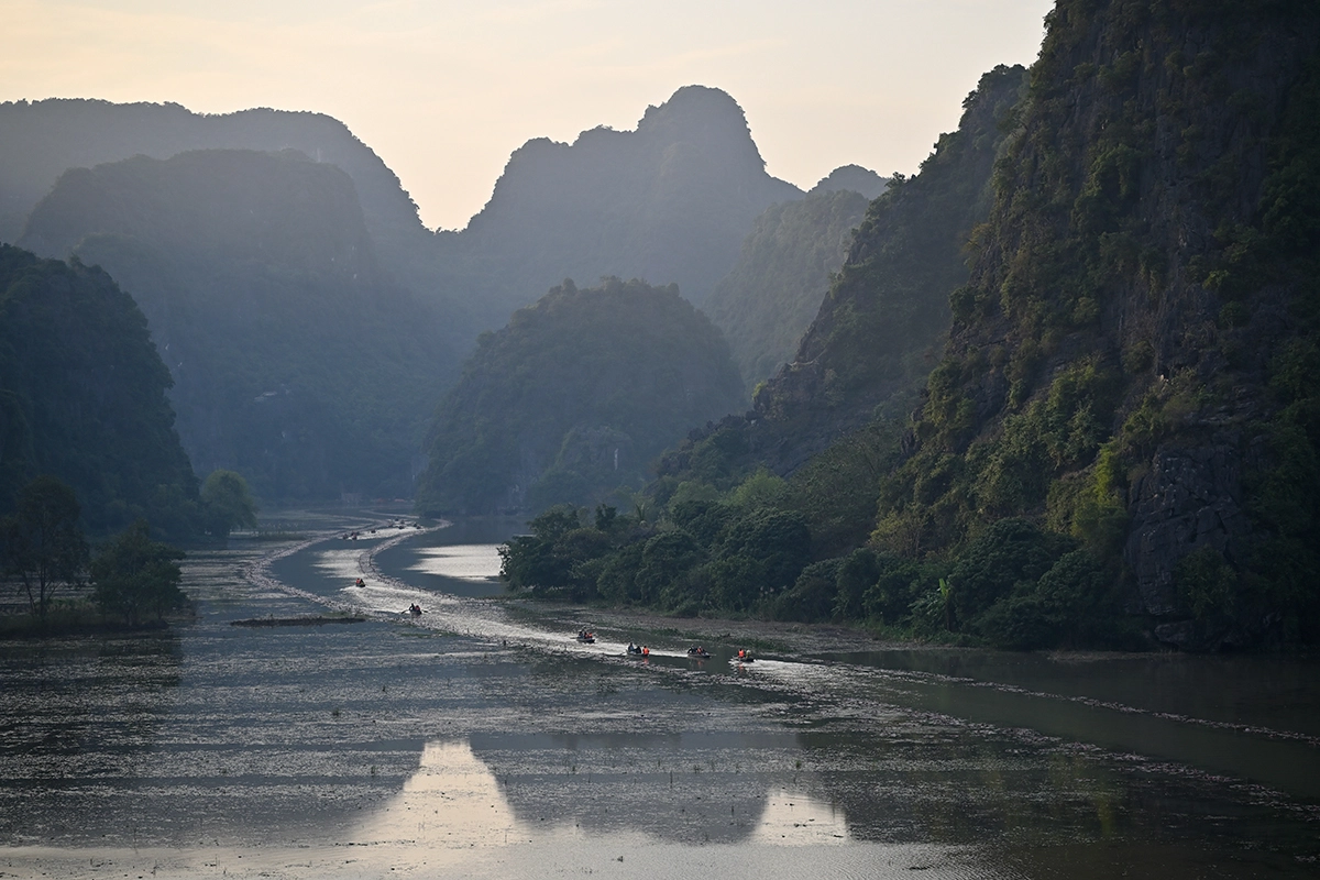 Barcos fluviais deslizando ao longo da hidrovia sinuosa de Tam Cốc ao pôr do sol, emoldurados por montanhas de calcário em camadas e luz atmosférica suave, fotografados com a Tamron 28-75 mm F2.8 G2.