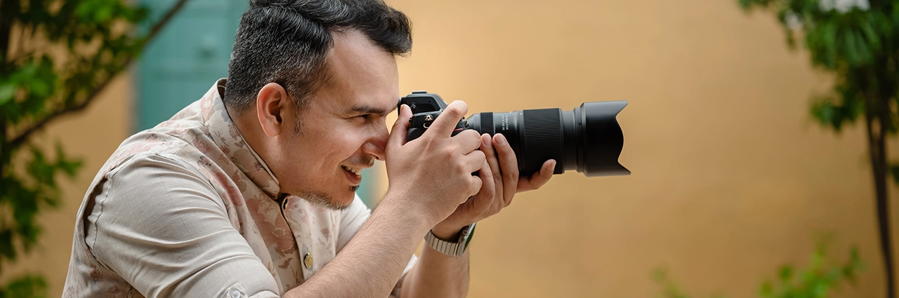 Photographer shooting outdoors with a mirrorless camera equipped with the Tamron 70-180mm F2.8 G2 lens, shown in a natural lifestyle environment.