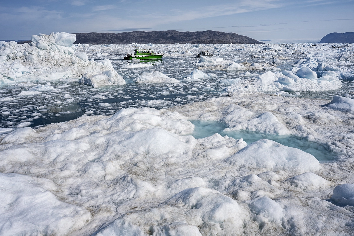 Barco verde navegando por aguas heladas rodeado de icebergs bajo la luz brillante del día.