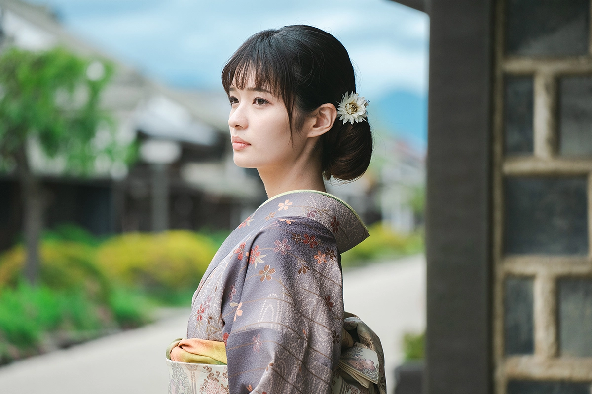 Mujer con un kimono tradicional de pie al aire libre con un fondo ligeramente desenfocado.