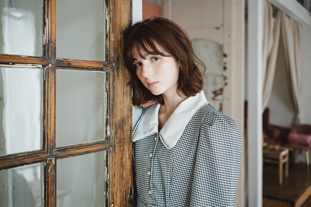 Retrato de uma mulher em um ambiente interno, encostada em uma moldura de porta de madeira, fotografada com uma lente Tamron de zoom rápido para montagem Nikon Z.