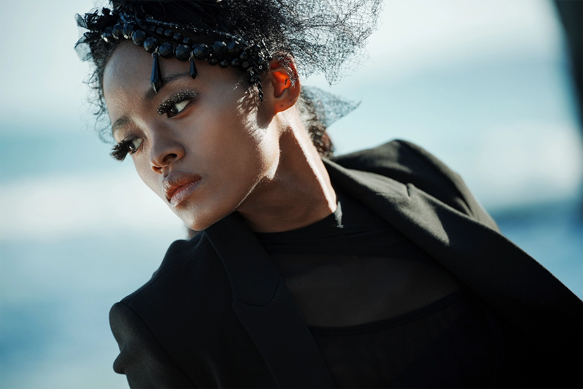 Retrato de una mujer con un atuendo negro y un tocado decorativo, fotografiada al aire libre con un suave desenfoque del fondo.