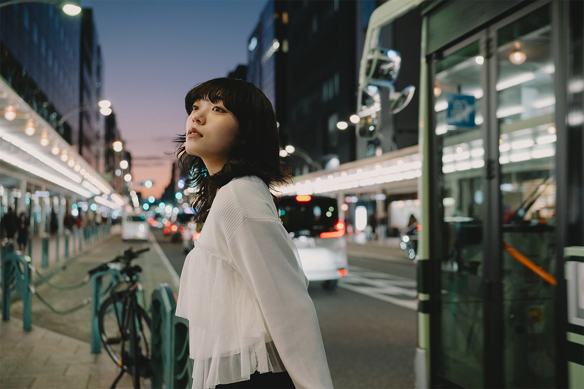 Foto de retrato de viagem de uma mulher em uma rua da cidade ao anoitecer com luzes de fundo suaves, capturada com uma lente de montagem Nikon Z.