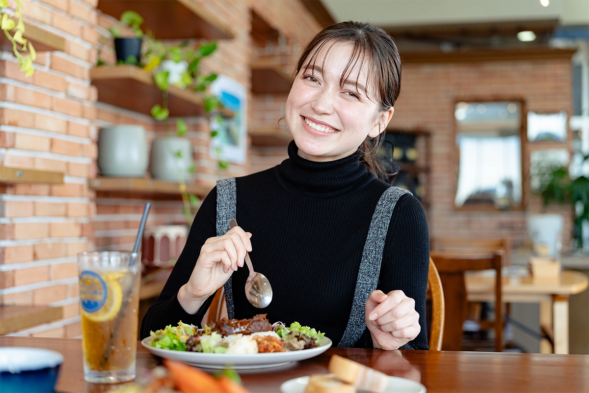 Woman smiling at a restaurant table captured with flattering 85mm portrait compression and soft natural background blur.