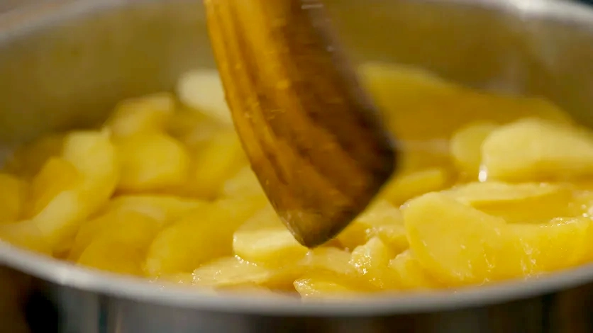 Close-up of a spatula stirring sliced apples in a pot with shallow depth of field for a cinematic food scene.