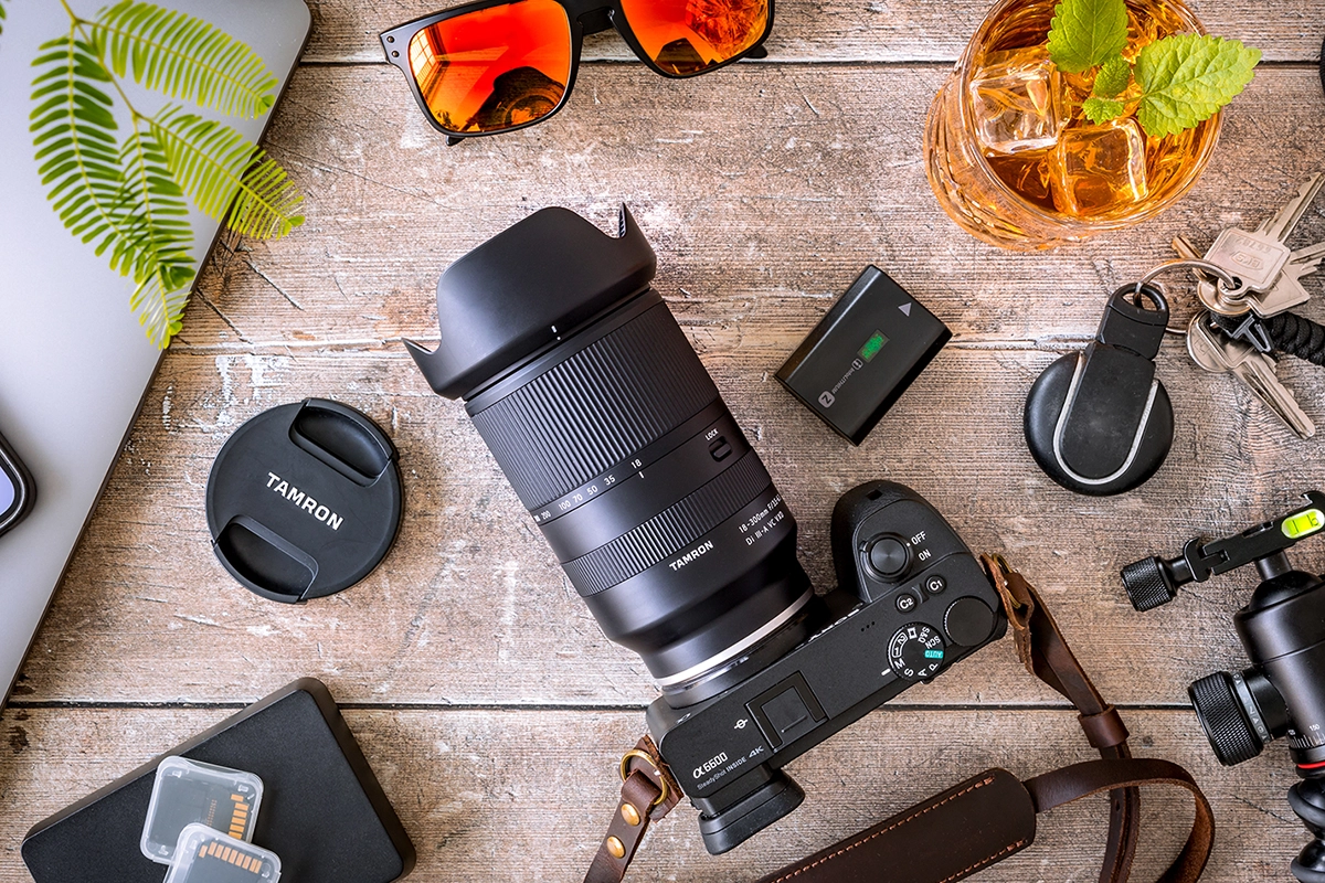 Objectif Tamron 18-300mm F/3.5-6.3 Di III-A VC VXD (modèle B061) monté sur un appareil photo sans miroir Sony APS-C sur une table avec des accessoires de voyage.