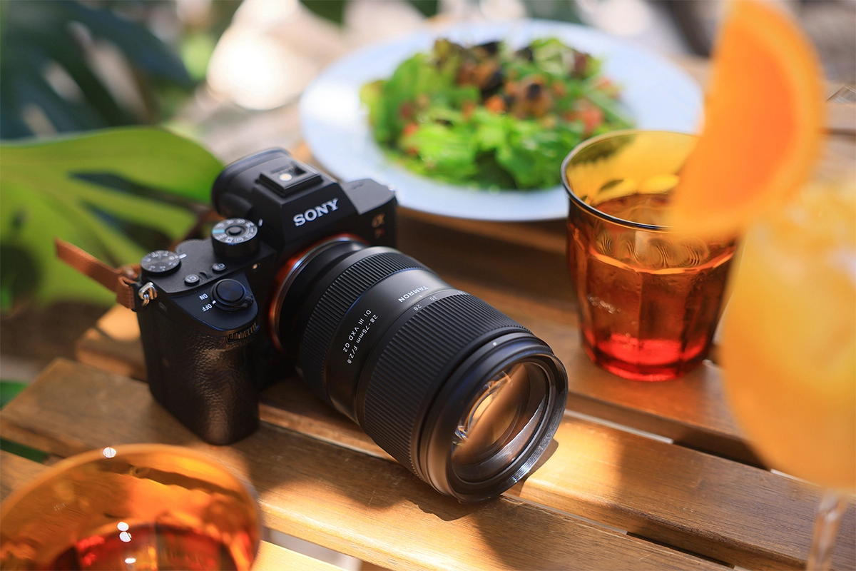 Objectif Tamron 28-75mm F/2.8 Di III VXD G2 (modèle A063) monté sur un appareil photo sans miroir Sony sur une table extérieure.