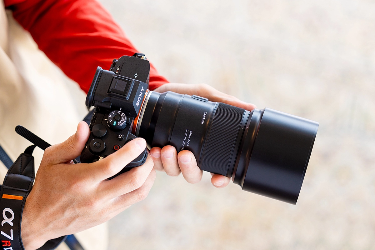 Objectif Tamron 90mm F/2.8 Di III VXD 1:1 Macro (modèle F072) monté sur un appareil photo sans miroir Sony tenu en main.