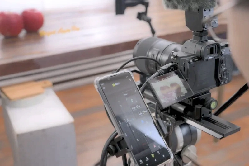 Behind-the-scenes view of a camera rig connected to a smartphone running Tamron Lens Utility Mobile.