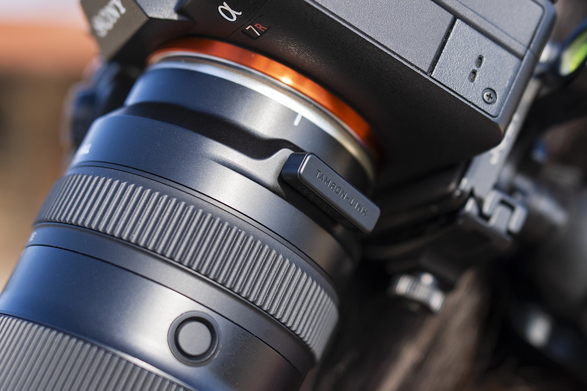 Gros plan d'un objectif sans miroir Tamron monté sur un appareil photo Sony avec le module sans fil TAMRON-LINK attaché, mettant en évidence la personnalisation à distance pour la photographie de nuit.