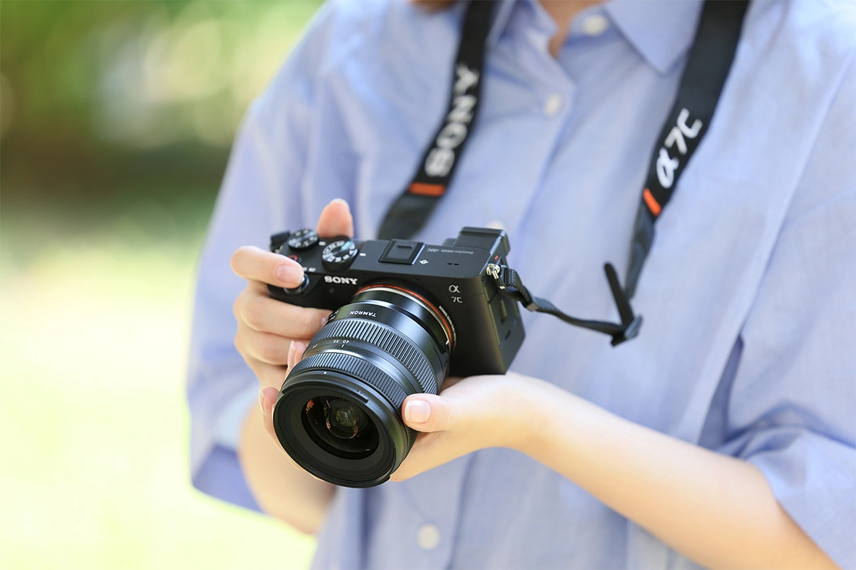 Objectif zoom standard Tamron monté sur un appareil photo sans miroir Sony a7C tenu par un photographe en extérieur.