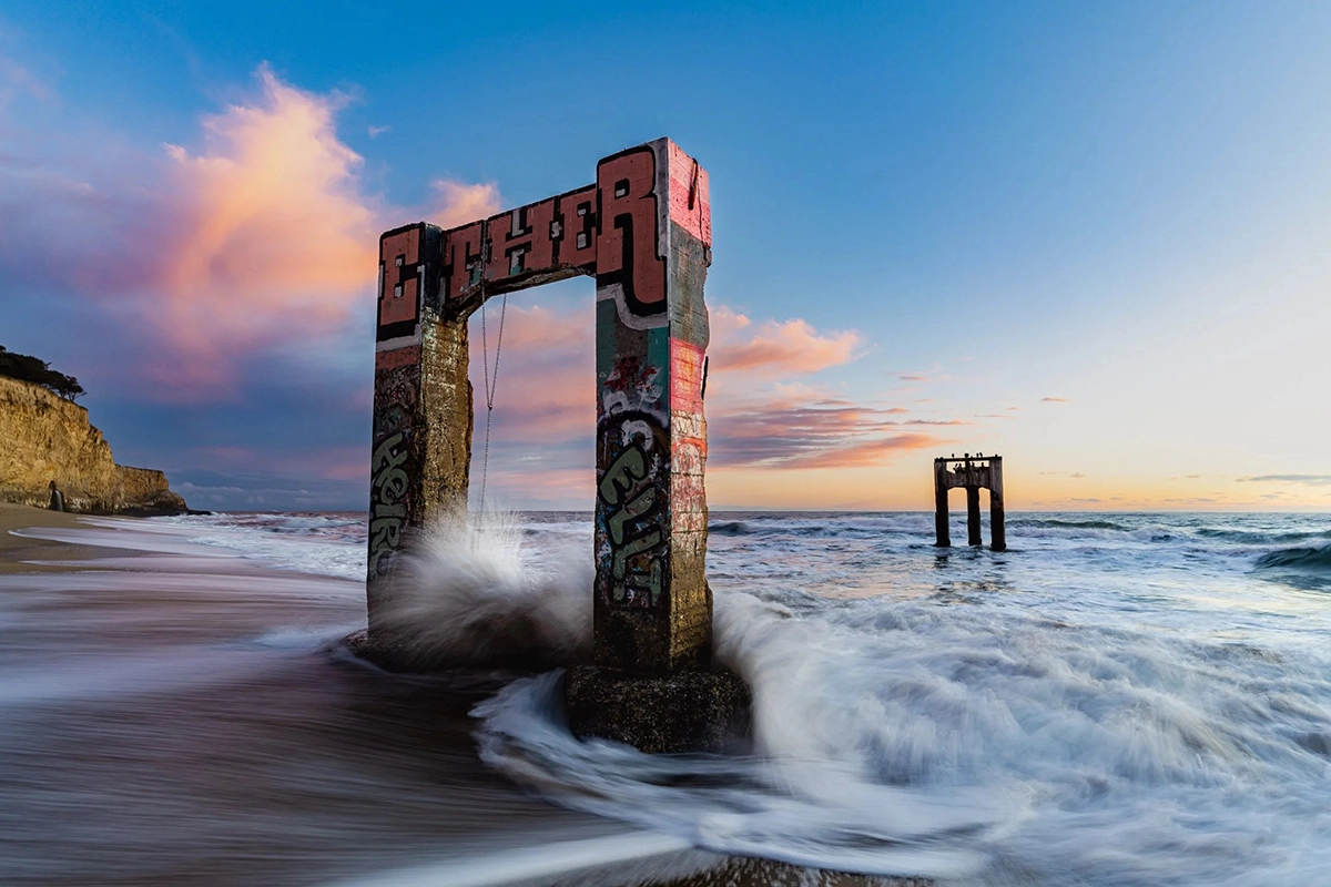Fotografía de un paisaje marino con olas del mar arremolinándose alrededor de una estructura costera al atardecer en Davenport, California.