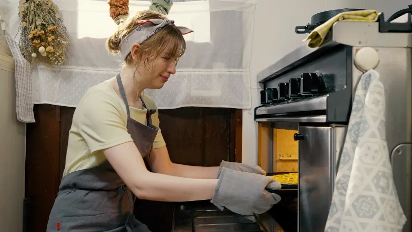 Woman placing a pie into an oven in a home kitchen.