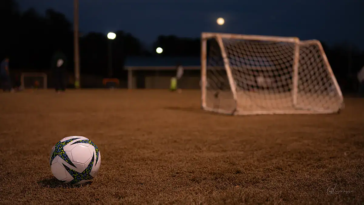 A lone soccer ball on the field with a soccer net nearby.