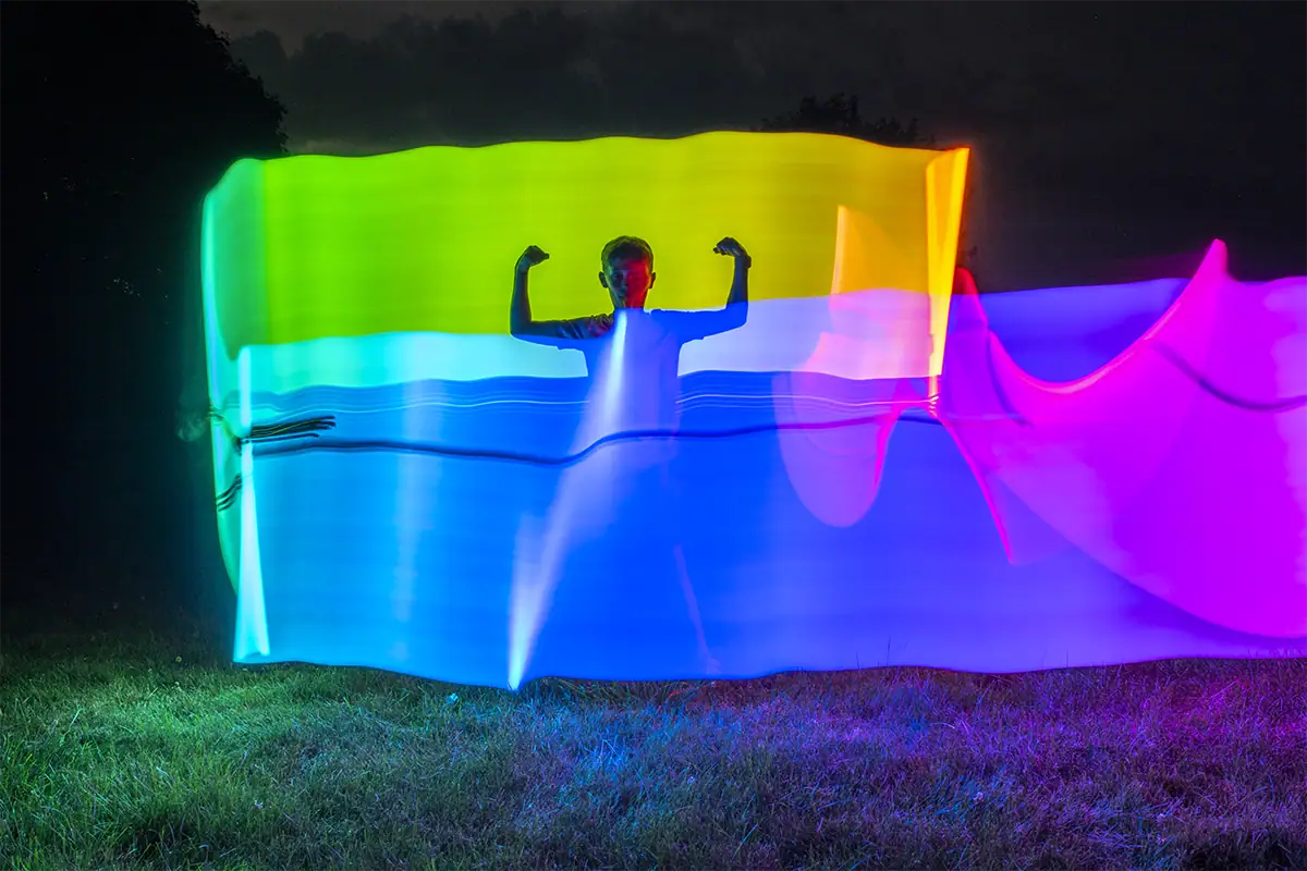 Silueta rodeada de coloridos rastros de luz en una escena nocturna de larga exposición.