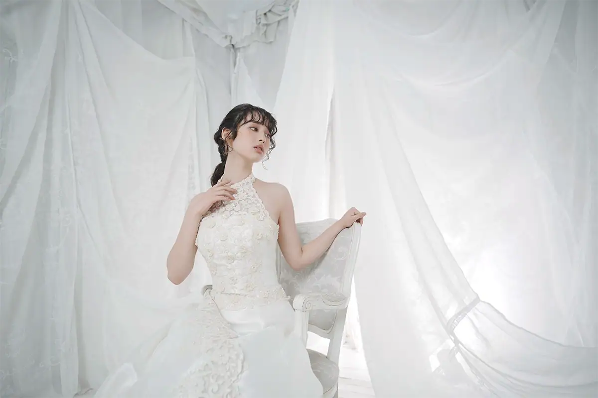 Bride seated in soft low-contrast light surrounded by white fabric for a moody portrait with gentle shadow and subtle depth.