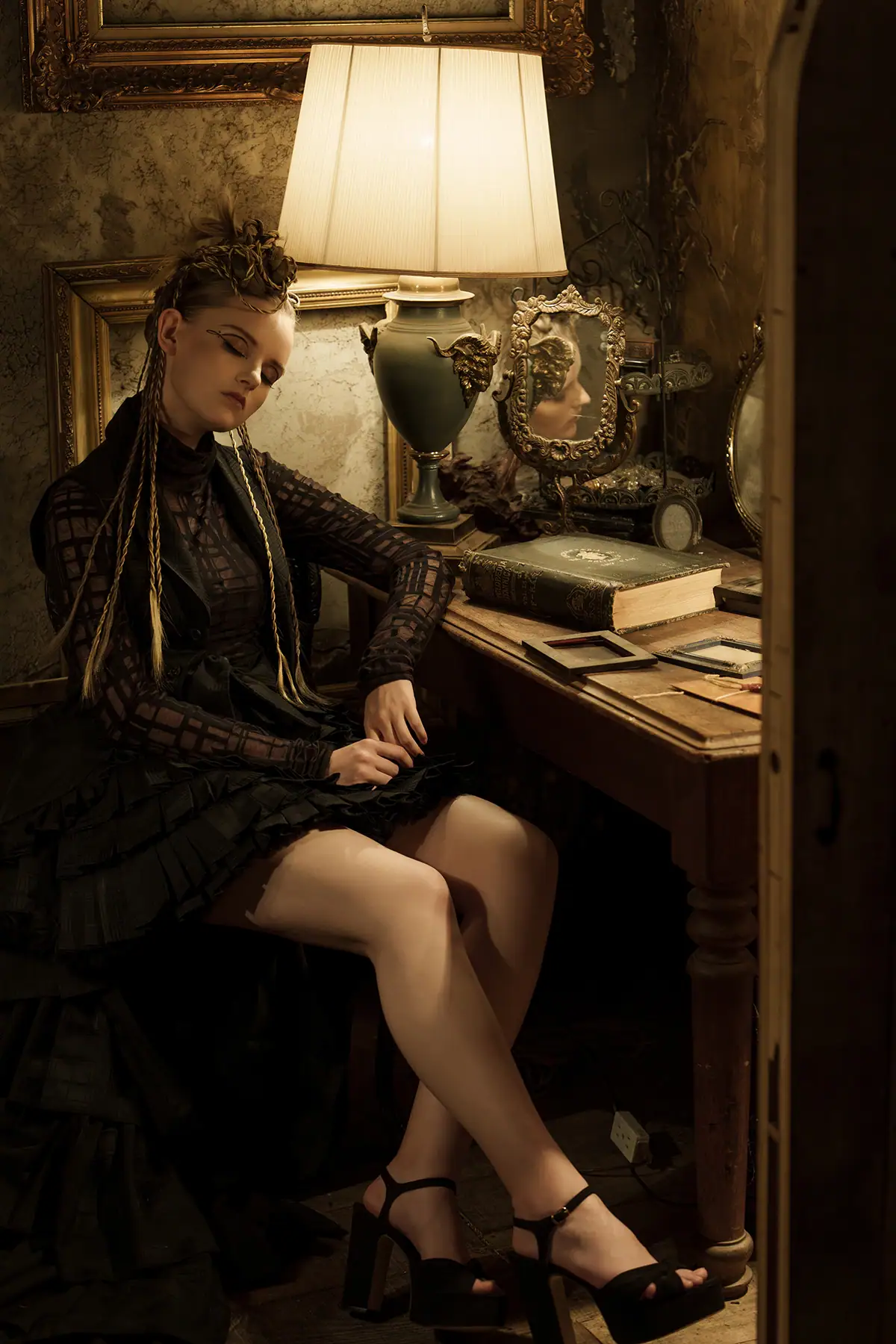 Woman seated at a vintage desk lit by a lamp in a moody portrait with warm practical light.