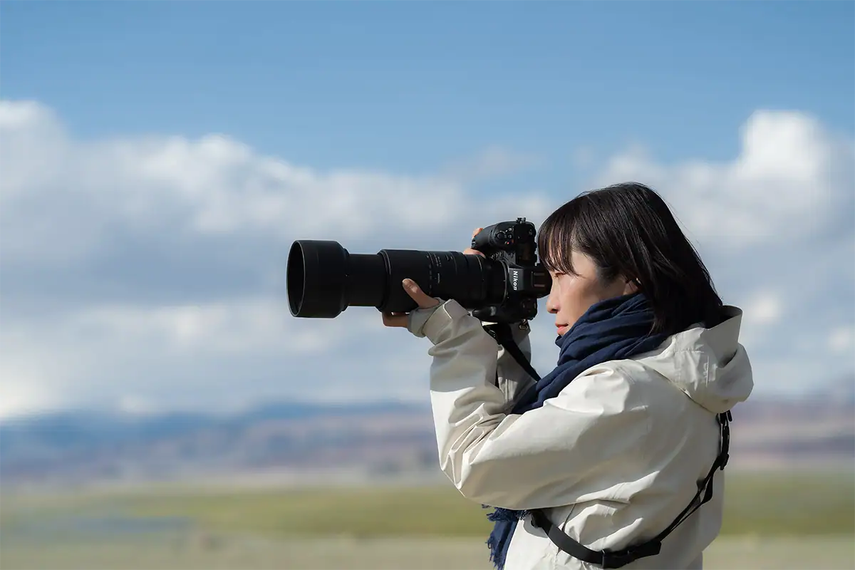 Fotógrafo usando uma lente telefoto para capturar a vida selvagem ao ar livre com um fundo de céu claro.