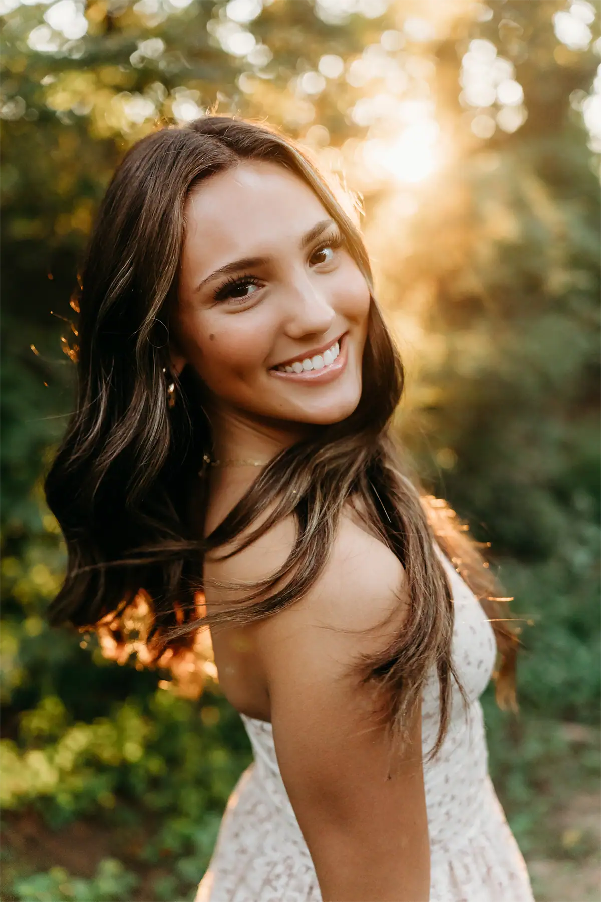 Una chica de último año de secundaria se gira hacia la cámara con una sonrisa natural, iluminada por una suave luz de fondo.